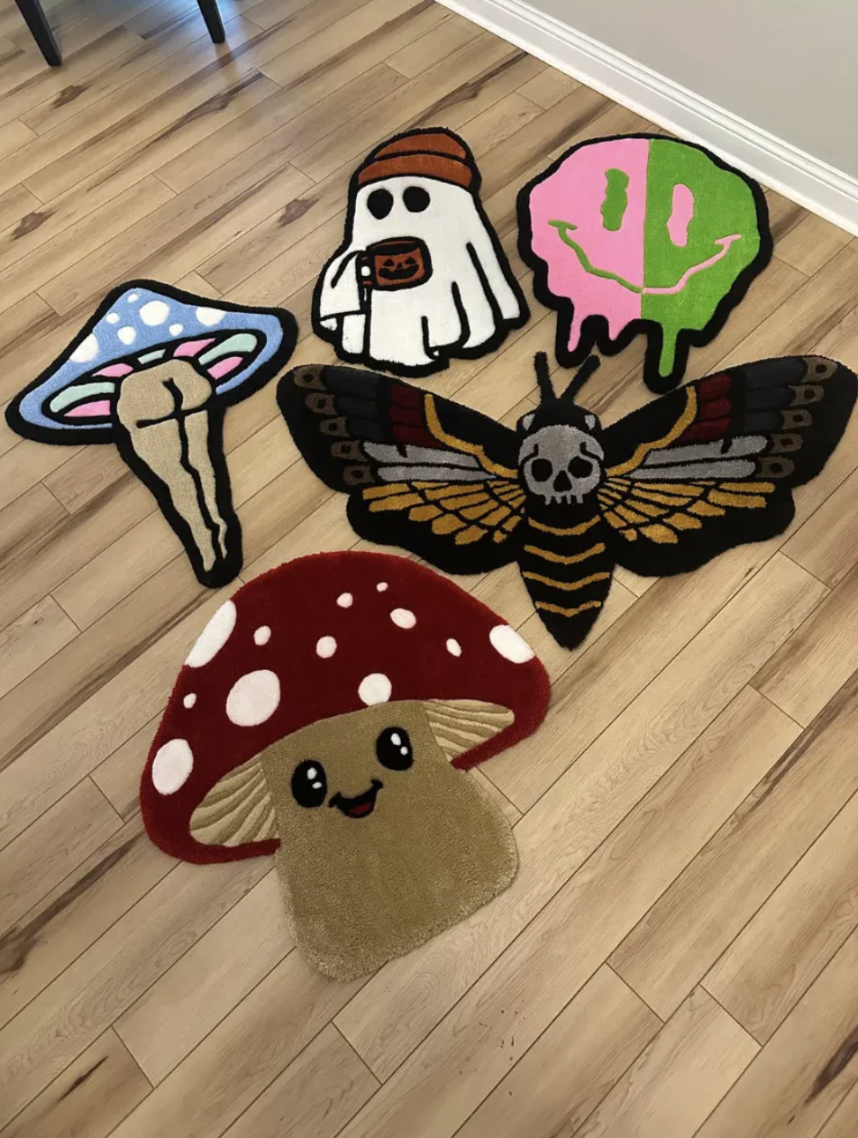 Five small shape rugs on a wooden floor: a ghost, a melting smiley, a mushroom, a moth and a smiling toadstool